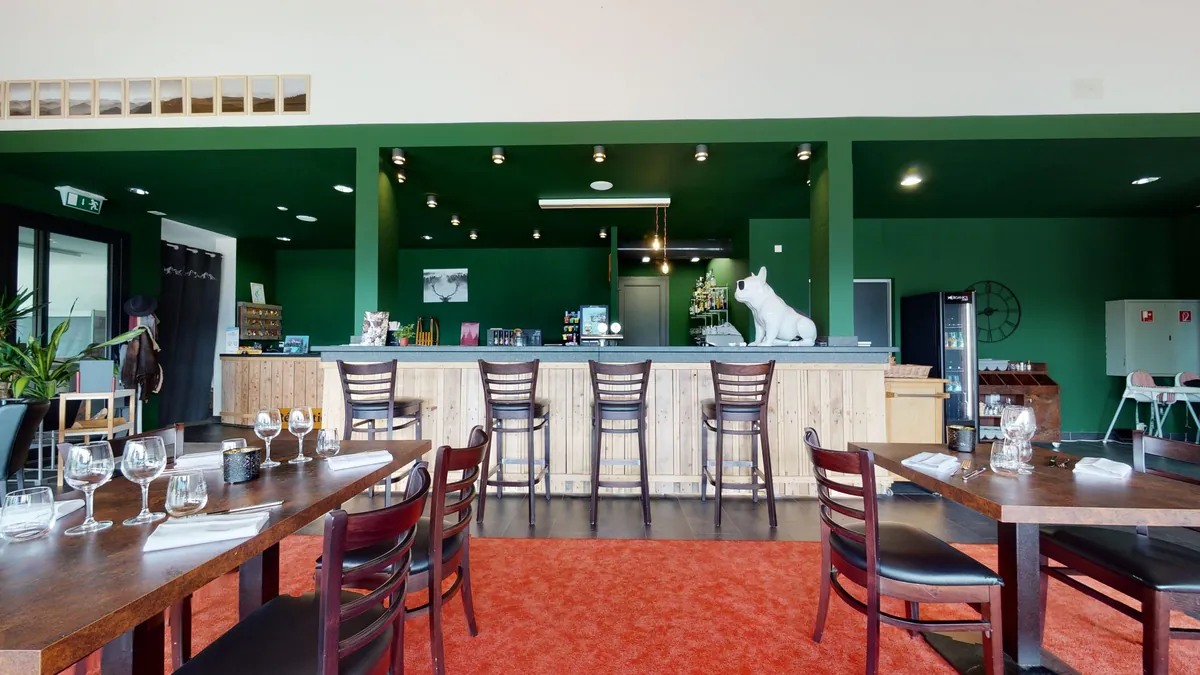 Le bar en bois clair du restaurant Woodland Village et son mur vert forêt